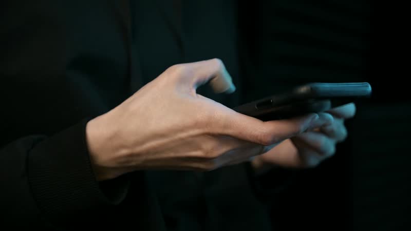 Close-up of two hands passing a mobile phone between them in low light.